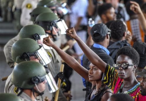 Ebonay Lee, center, and another unidentified woman holds up their fists in front of a line of police and protesters, Wednesday, Sept. 28, 2016, in El Cajon, Calif. Dozens of demonstrators on Wednesday protested the killing of a black man shot by an officer after authorities said the man pulled an object from a pocket, pointed it and assumed a "shooting stance."