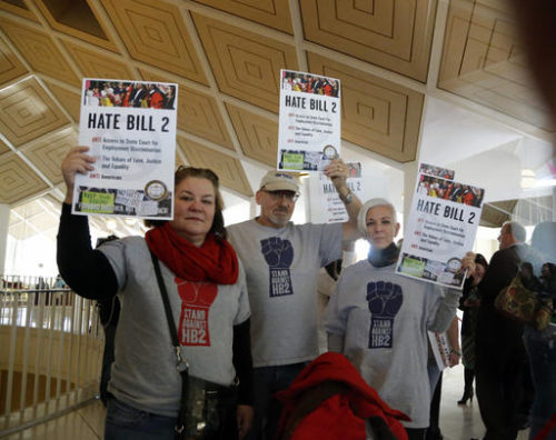 FILE - In a Dec. 21, 2016 file photo, opponents of House Bill 2 hold signs outside the House chambers gallery as the North Carolina General Assembly convenes for a special session at the Legislative Building in Raleigh, N.C. Atlantic Coast Conference Commissioner John Swofford says Sunday, Jan. 8, 2017, that the conference is likely to move its football championship game out of Charlotte, North Carolina, again if a state law that limits anti-discrimination protections for LGBT people is not repealed or adjusted.
