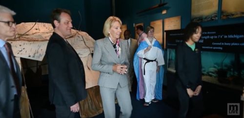 When Education Secretary Betsy DeVos visited Torin Hodgman's school, they made sure she saw trans representation. Betsy DeVos tours a school while Torin Hodgman wears a trans flag in the background.