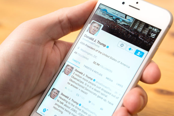 Phone in hand with the official Twitter account of Donald Trump on screen.
