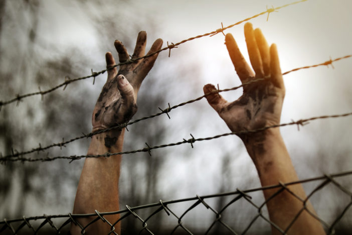 Two dirty hands clutch at a barbed wire fence