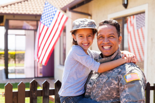 A Latino US Army soldier holds his daughter in front of his home
