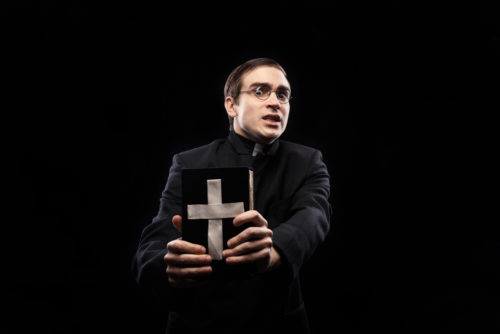 Portrait of frightened young catholic priest against black background
