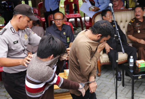 A police officer escort two men convicted of gay sex to be publicly caned at a mosque in Banda Aceh, Aceh province Indonesia, Tuesday, May 23, 2017. The two men were publicly caned dozens of times Tuesday for consensual sex, a punishment that intensifies an anti-gay backlash and which rights advocates denounced as "medieval torture." (AP Photo/Heri Juanda) Two men trying to cover their faces, being led by a police officer.