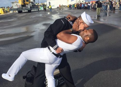 Two men kissing, one is a sailor.