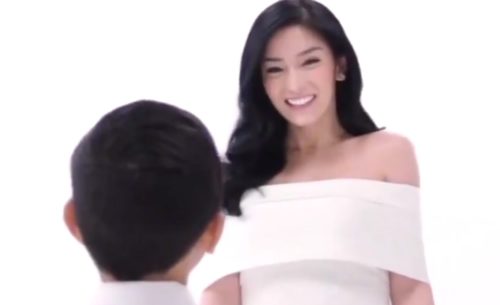 A smiling woman in white looks at a child with short hair..