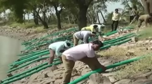 Several people holding green pipes next to a lake with trees in the background.