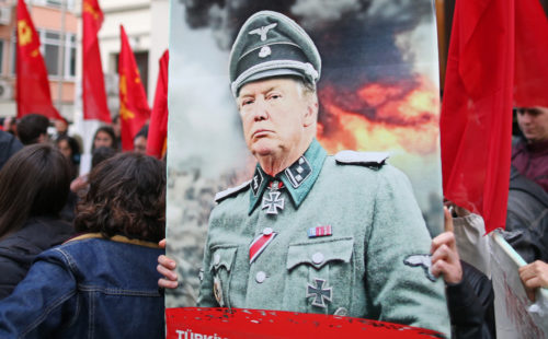 ISTANBUL, TURKEY, 14 APRIL 2018. A protestor hold picture of US President Donald J. Trump with Nazi uniform during a protest against the United States. ISTANBUL, TURKEY, 14 APRIL 2018. A protestor hold picture of US President Donald J. Trump with Nazi uniform during a protest against the United States.