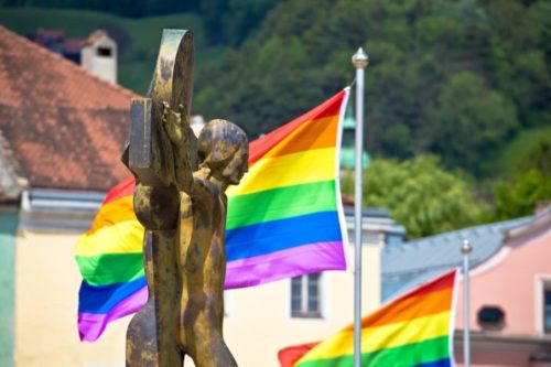 A crucifix and rainbow flags in the background