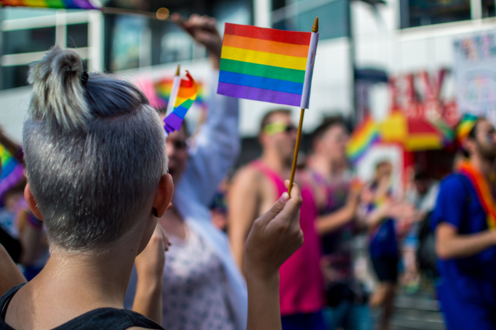 A woman with a buzzcut waving a small rainbow LGBT, or Queer, pride flag at a march.