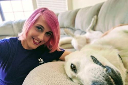 Hailie, a USAA transgender employee with pink hair, poses with her yellow lab on a couch.