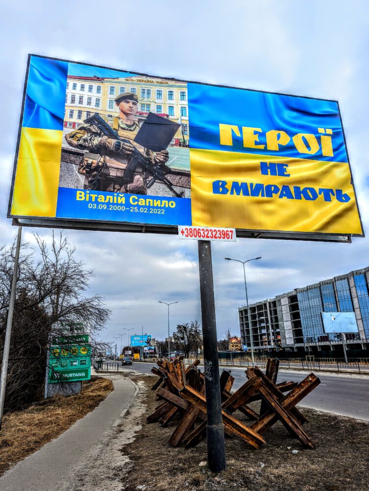 3/13/22: A billboard, towering over anti-tank spikes, offering a memorial to a fallen Ukrainian Armed Forces member in Lviv 