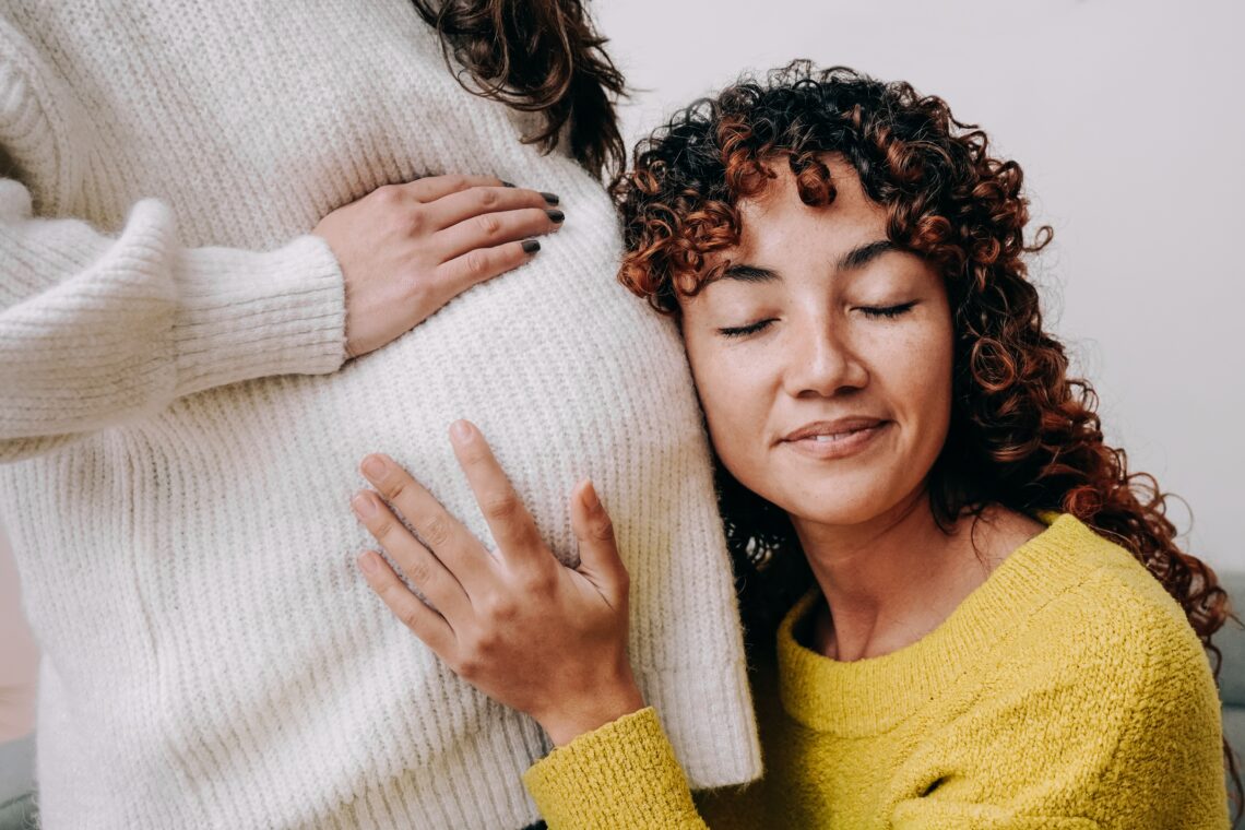 LGBT lesbian pregnant woman having tender moment listening her wife baby belly - Focus on right female 